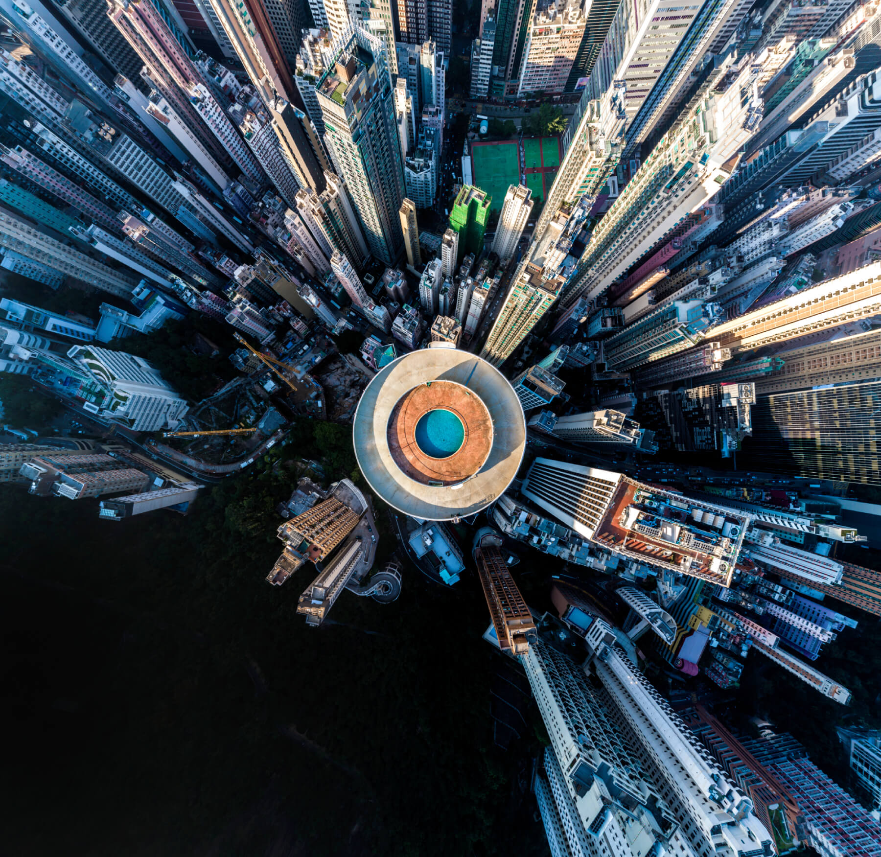 Aerial view of a city with dense high-rise buildings, centred around a tall building with a circular rooftop helipad.