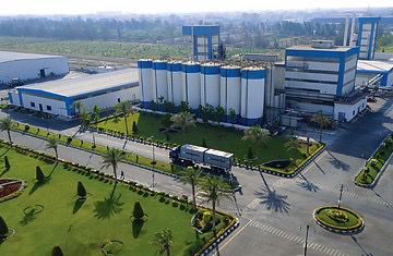 Aerial view of an industrial facility with white storage silos, a lorry, landscaped lawns, and surrounding roads.